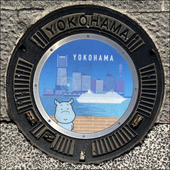 manhole cover - Moomin in forgraound backed by a cruise ship and Yokohama city skyline - mainly coloured in shades of blue